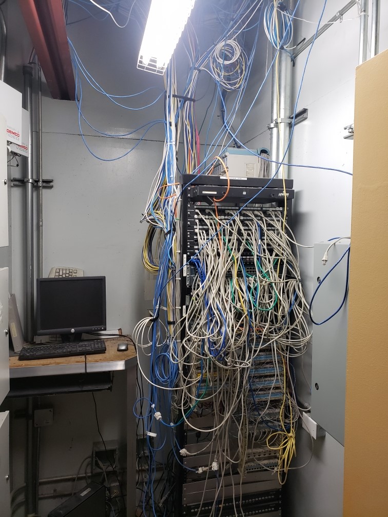 Overhead cabling tangled above an open server rack before a Capilano Communications cleanup